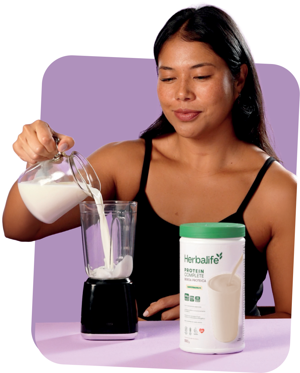 Mulher despejando leite no liquidificador ao lado do pote de Protein Complete